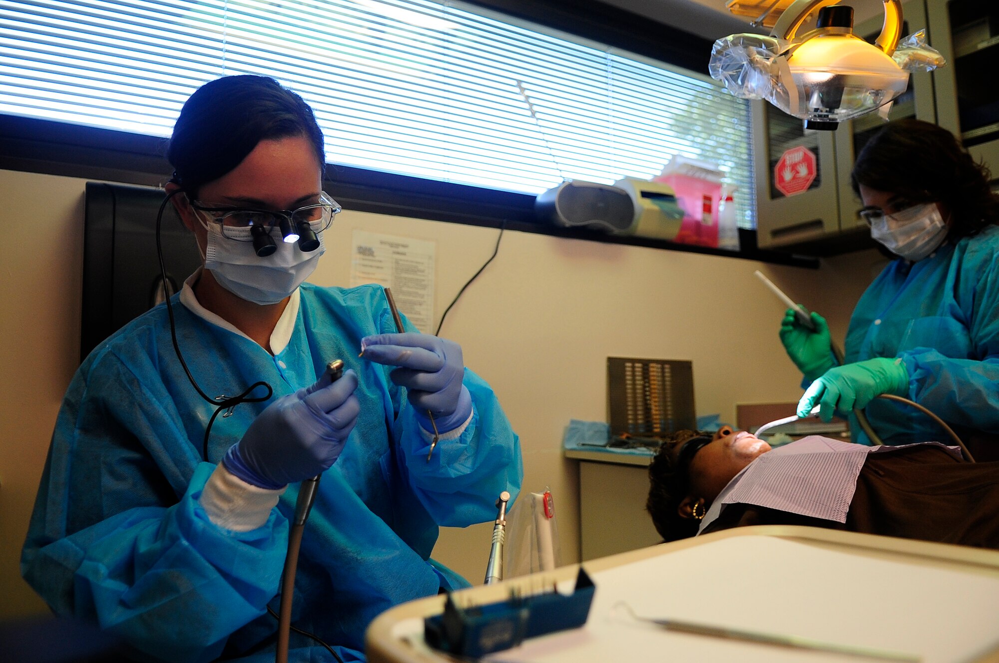 U.S. Air Force Capt. Jennilyn Estell, 20th Dental Squadron doctor of medical dentistry, prepares an instrument for use while Sunshine Maldanado, dental assistant, works on patient Tanya Maisonet during a training exercise for the Red Cross Volunteer Dental Assistance Program, Shaw Air Force Base, S.C., Sept. 24, 2012. The Red Cross Dental Assistance Program offers dental education to military dependents and spouses, with over 900 hours of both classroom and hands-on training. (U.S. Air Force photo by Airman Hunter Brady/Released) 
