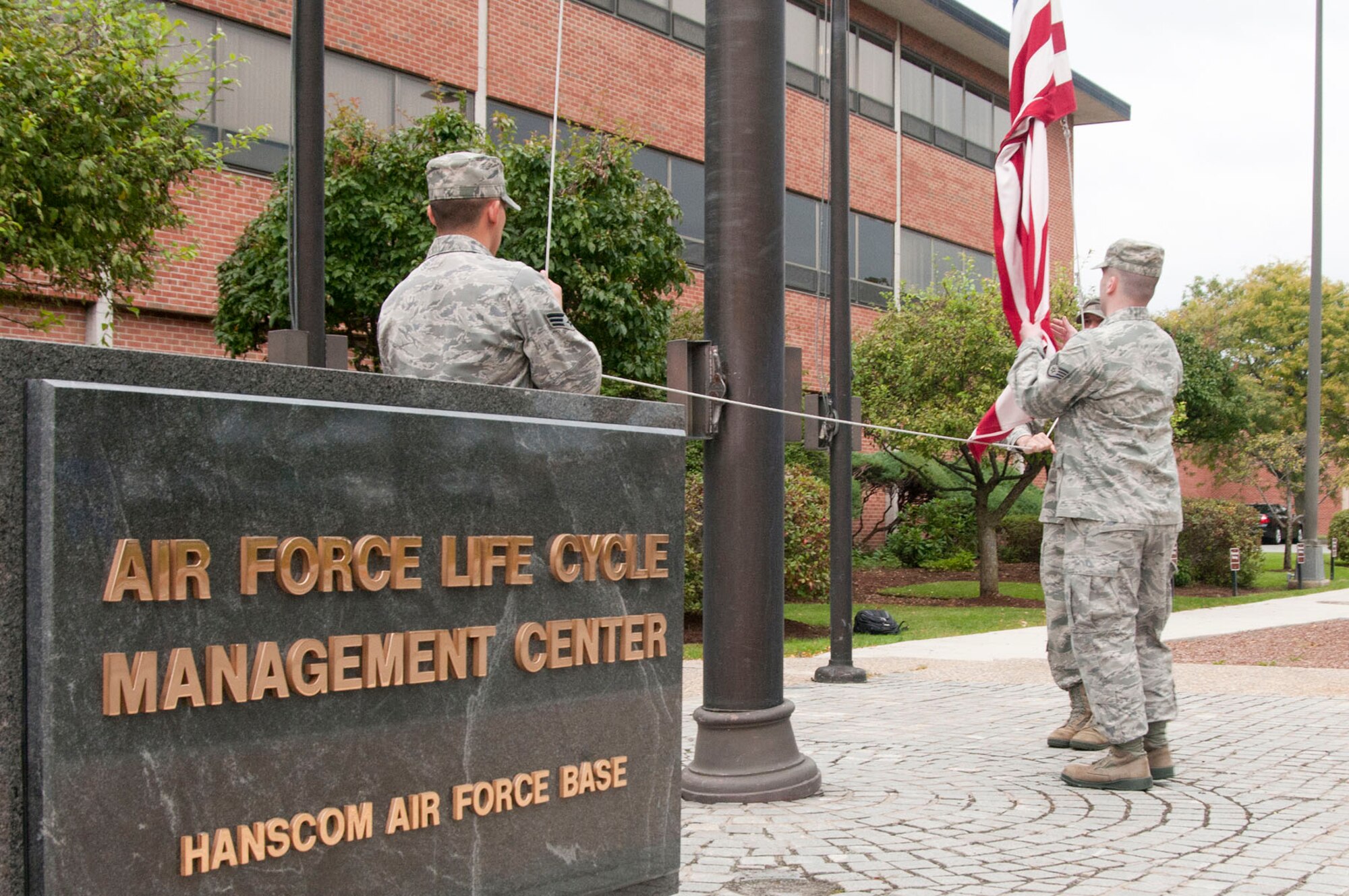 HANSCOM AIR FORCE BASE, Mass. -- Senior Airman Matthew Ramos, Staff Sgt. Jeremiah Schroeder and Airman 1st Class Jason Walker, all from the Air Force Life Cycle Management Center, retrieve the flag during a retreat ceremony outside Building 1606 Sept. 26. Members of AFLCMC participated in a formation and the U.S. Air Force Band of Liberty performed the national anthem during the monthly formal ceremony. (U.S. Air Force photo by Mark Wyatt)