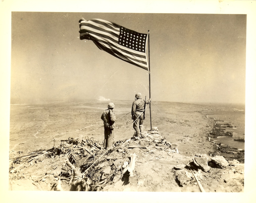 Raised flag on Mount Suribachi, LST's lined up along the assault beaches to the right, the rest of Iwo Jima stretches out in the distance to the left.