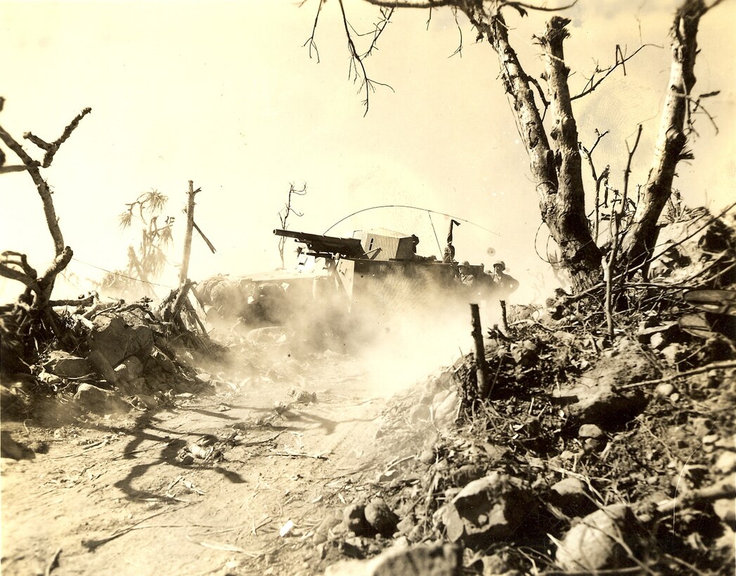 A self propelled artillery vehicle fires at Japanese defensive positions. At far right is a DR-5 wire reel, communications wire is strung from the trees and ground.