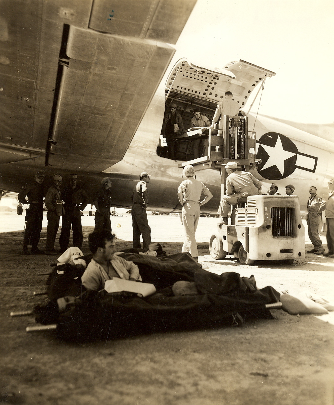 Wounded Marines lay on stretchers waiting to be loaded on to aircraft for evacuation, a forklift is used to load the stretchers.
