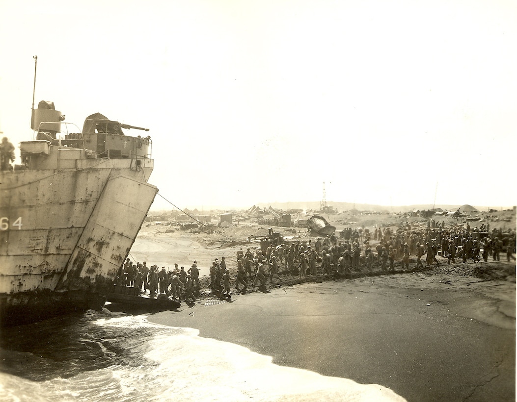 An LST loads/unloads at left, Marine operations on landing beaches in background.