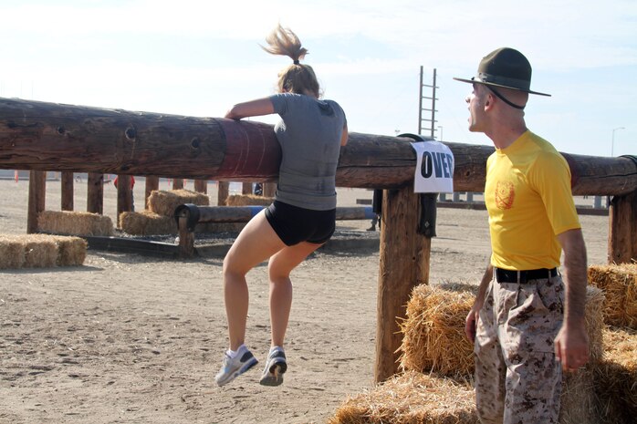 Sgt. Joseph A. Onello, drill instructor, Company G, 2nd Recruit Training Battalion, motivates a runner as she attempts to climb over a log during the 11th annual Boot Camp Challenge Sept. 29 aboard Marine Corps Recruit Depot San Diego. The Boot Camp Challenge is a three-mile course that featured 52 obstacles that included walls, logs, trenches, and push-up stations. 60 MCRD drill instructors were placed throughout the course to help instruct and encourage participants over the obstacles.
