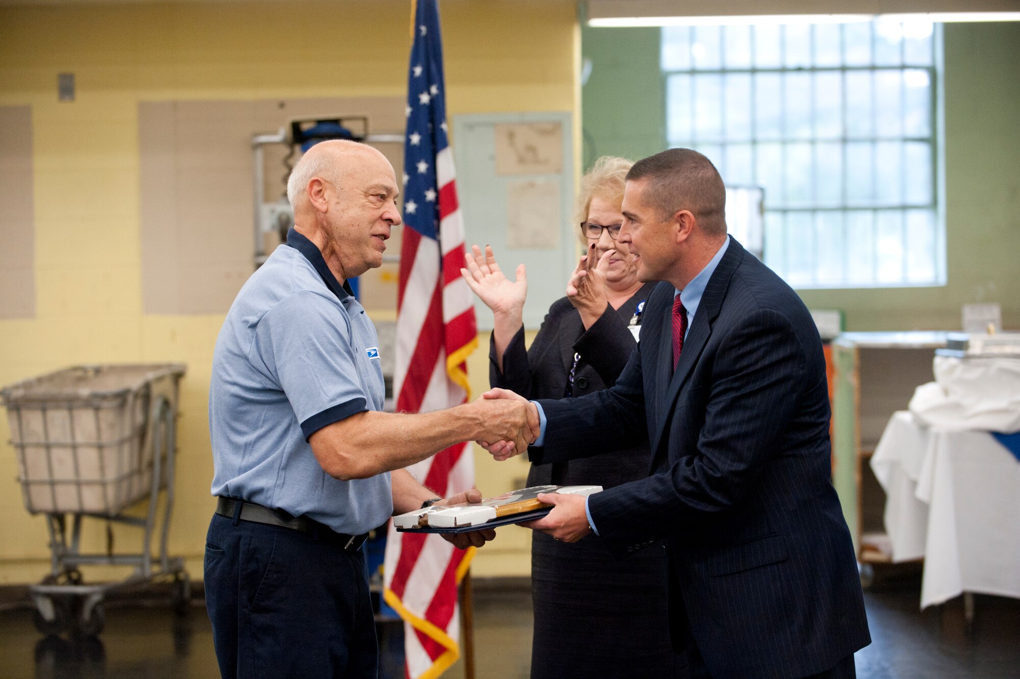 Linda Malone, South Jersey District Manager looks on while Keith Heck, Postmaster Trenton, congratulates Gary Frese, United States Postal Service worker, for fifty years of service Oct. 4 in the Fort Dix Post Office at Joint Base-McGuire-Dix-Lakehurst, N.J. Frese entered the USPS in 1962 and transferred to then Fort Dix in 1978. He was presented a South Jersey Performance Cluster, a  recognition of service certificate, and a 50-year pin.  (U.S. Air Force photo by Russ Meseroll/Released)