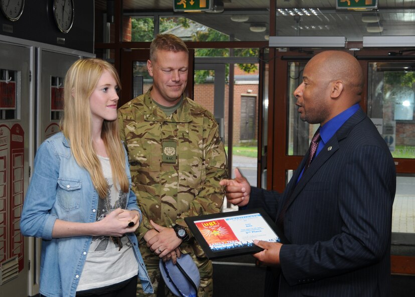 Moses Thompson, right, 100th Force Support Squadron deputy director of manpower, personnel and services, presents a second-place Air Force-level “You Got Talent” award to Emily Bate, left, as her father, Army Air Corps Chief Warrant Officer 2 Rick Bate, assigned to Wattisham Airfield, looks on Oct. 4, 2012, at RAF Mildenhall, England. Bate won the award in the Teen (13-18) Solo Performance/Specialty Act category and competed against peers from across the Air Force. (U.S. Air Force photo by Tech. Sgt. Neal X. Joiner/Released) 