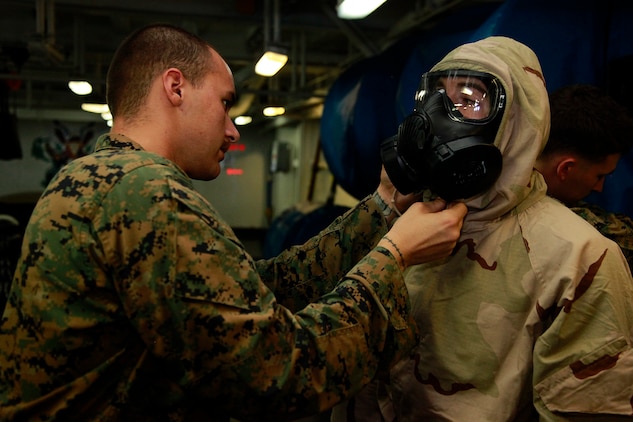 Lance Cpl. Anthony C. Bocz, assessment consequence management team member, Chemical, Biological, Radiological and Nuclear Defense Platoon, 15th Marine Expeditionary Unit, adjusts the M50 field protective mask on a Marine from Weapons Company, Battalion Landing Team 3/5, 15th MEU, during a class on CBRN defense aboard the USS Peleliu, Oct. 4. The 15th MEU?s CBRN Defense Platoon is spending an entire month preparing the 2,400 servicemembers that make up the MEU on how to properly operate in contaminated environments. The 15th MEU is currently embarked as part of the Peleliu Amphibious Ready Group, while they serve as the nation's rapid-response sea-based Marine Air Ground Task Force for Western Pacific Deployment 12-02. Bocz, 20, is from Sacramento, Calif.::r::::n::