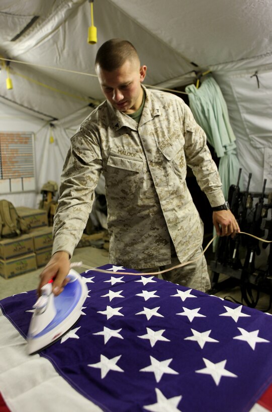 Lance Cpl. Alexander F. Maloof, from McLean, Va., a personnel retrieval and processing specialist with the Personnel Retrieval and Processing Detachment, 2nd Marine Logistics Group (Forward) irons a flag July 13, 2011, aboard Camp Dwyer, Afghanistan. Marines with the Personnel Retrieval and Processing Detachment, 2nd Marine Logistics Group (Forward) at Camp Dwyer, Afghanistan, are on call 24 hours a day, seven days a week to take care their own in Southern Helmand province and bring them home.