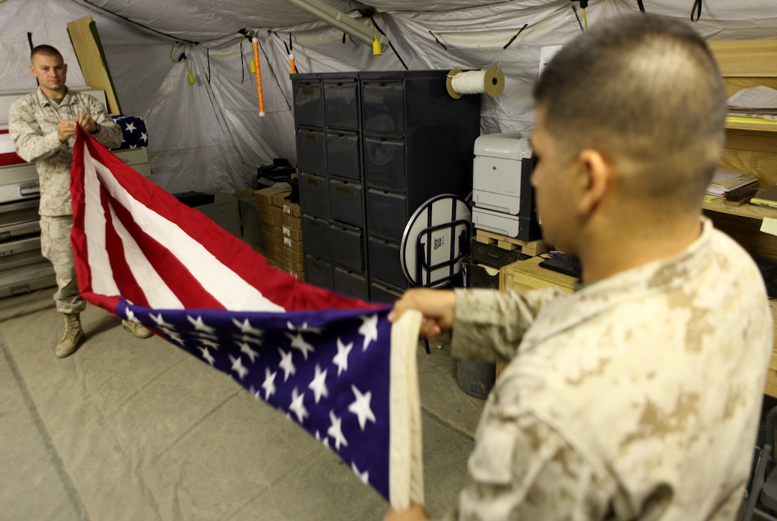 Lance Cpl. Alexander F. Maloof (background), from McLean, Va., and Lance Cpl. Kevin E. Campos (foreground), from Sacramento, Calif., both personnel retrieval and processing specialists with the Personnel Retrieval and Processing Detachment, 2nd Marine Logistics Group (Forward) fold a flag July 13, 2011, aboard Camp Dwyer, Afghanistan. Marines with the Personnel Retrieval and Processing Detachment, 2nd Marine Logistics Group (Forward) at Camp Dwyer, Afghanistan, are on call 24 hours a day, seven days a week to take care their own in Southern Helmand province and bring them home.