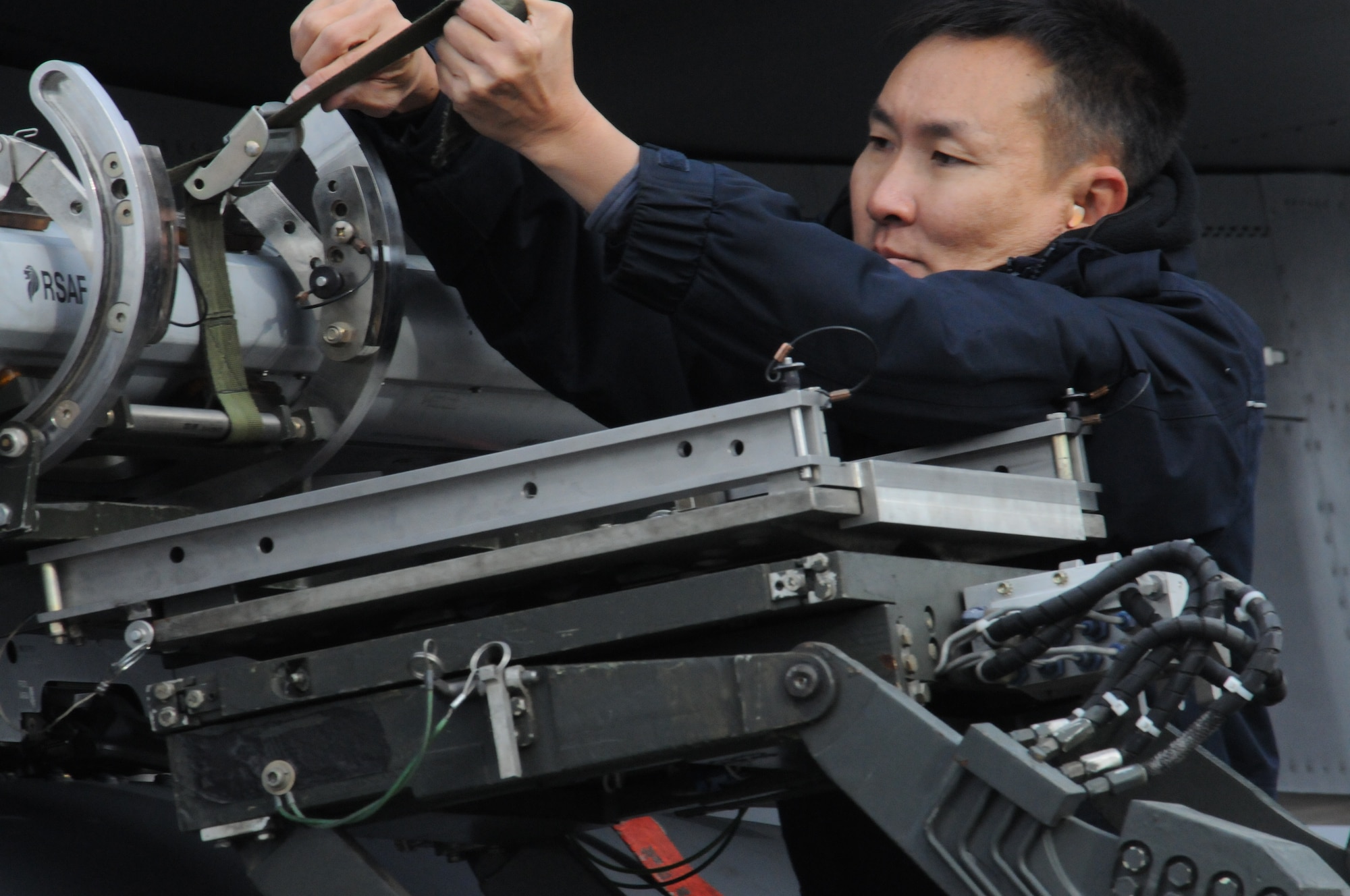 ME2 Sze Fang Siang, 428th Fighter Squadron weapon number 1 man, tightens a strap securing a munition Oct. 5, 2012, at Eielson Air Force Base, Alaska. Personnel from the 428th FS are practicing and preparing for the RED FLAG-Alaska 13-1 exercise which begins next week. (U. S. Air Force photo/Senior Airman Benjamin Sutton)