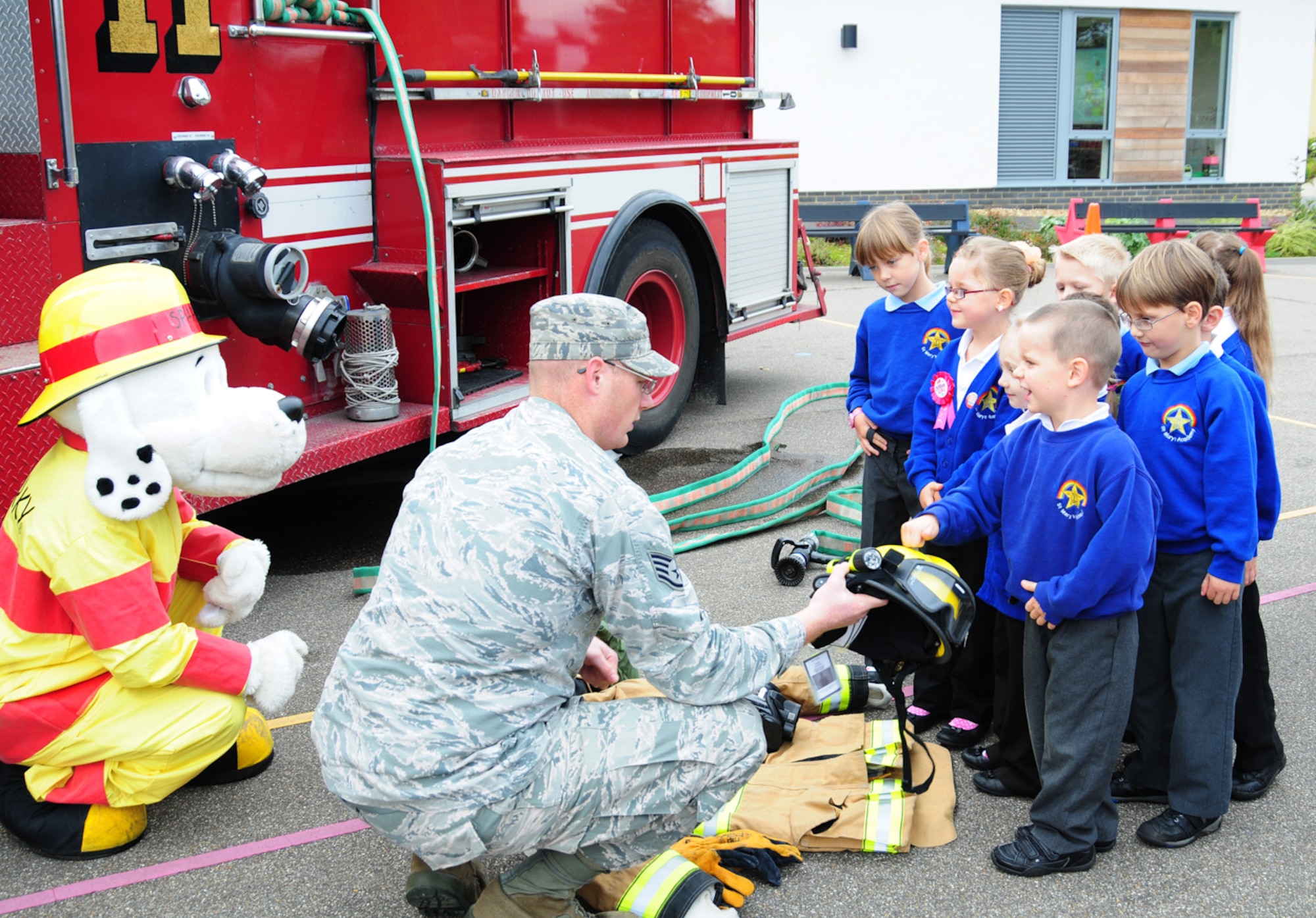 Sparky the Fire Dog and Staff Sgt. William Pritchett, 100th Civil Engineer Squadron Fire Department, RAF Mildenhall, show a set of protective clothing to children at St. Mary's Academy, Mildenhall, England, Oct. 8, 2012. As part of Fire Prevention Week, firefighters from RAF Mildenhall visited the school, along with Beck Row Primary School, to talk to the children about how to get out of the house safely in the event of a fire. (U.S. Air Force photo/Karen Abeyasekere)