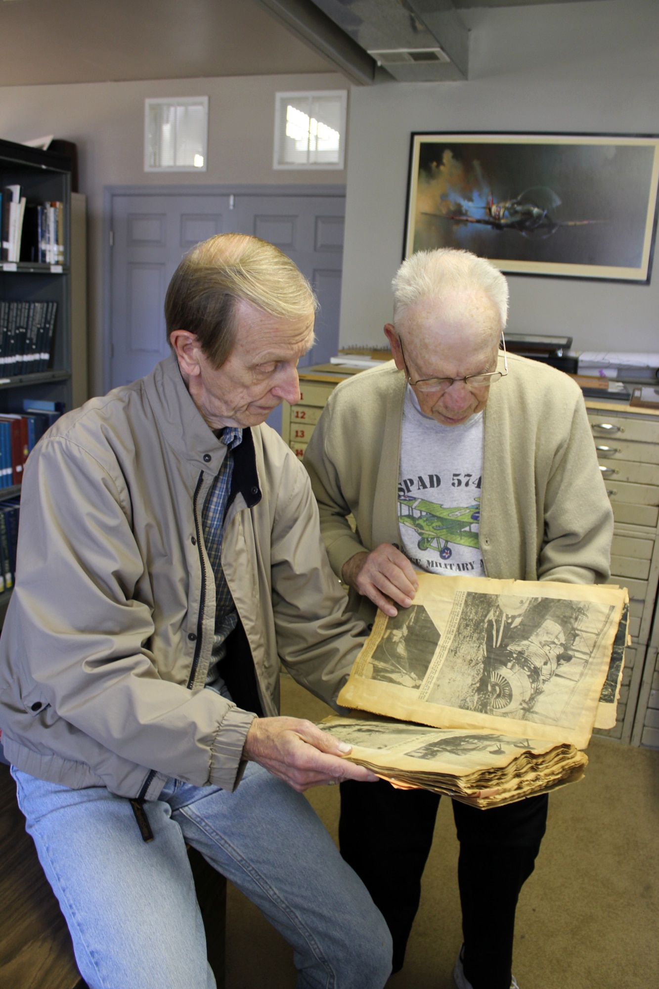 Dick Soules, left, and Frank Brown look at an old scrap book, possibly kept by a child in the 1930s, that is filled with newspaper clippings and other items that track the development of aviation. The scrapbook is a part of the collection of historical materials in the library of the Selfridge Military and Air Museum at Selfridge Air National Guard Base, Mich. The two men are among a group of a half dozen or so museum volunteers who are working on cataloging the various items that exist at the museum, such as the scrapbook. The two men were working at the museum on Oct. 9, 2012. (Air National Guard photo by TSgt. Dan Heaton)