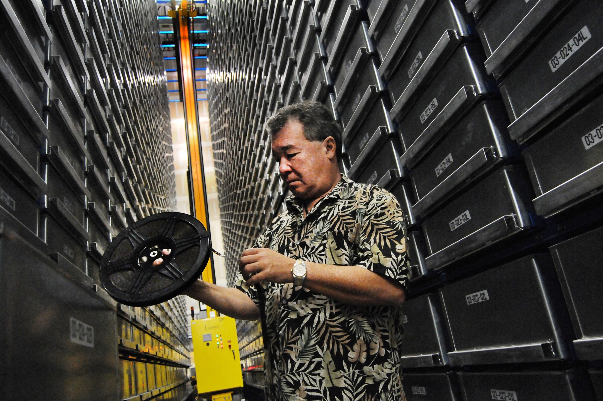 Dr. Pedro Loureiro checks a film reel at the automated search and retrieval system at the Defense Imagery Management Operations Center-Riverside, Calif., Oct. 9, 2012. Loureiro, the archivist at DIMOC-R, helped find a film reel containing clips of the Tonight Show starring Johnny Carson. The ASRS  has about 280,000 analog tapes, 80,000 rells of 16mm and 35mm film and 40,000 negatives, slides and photos in storage. (U.S. Air Force photo/Val Gempis)