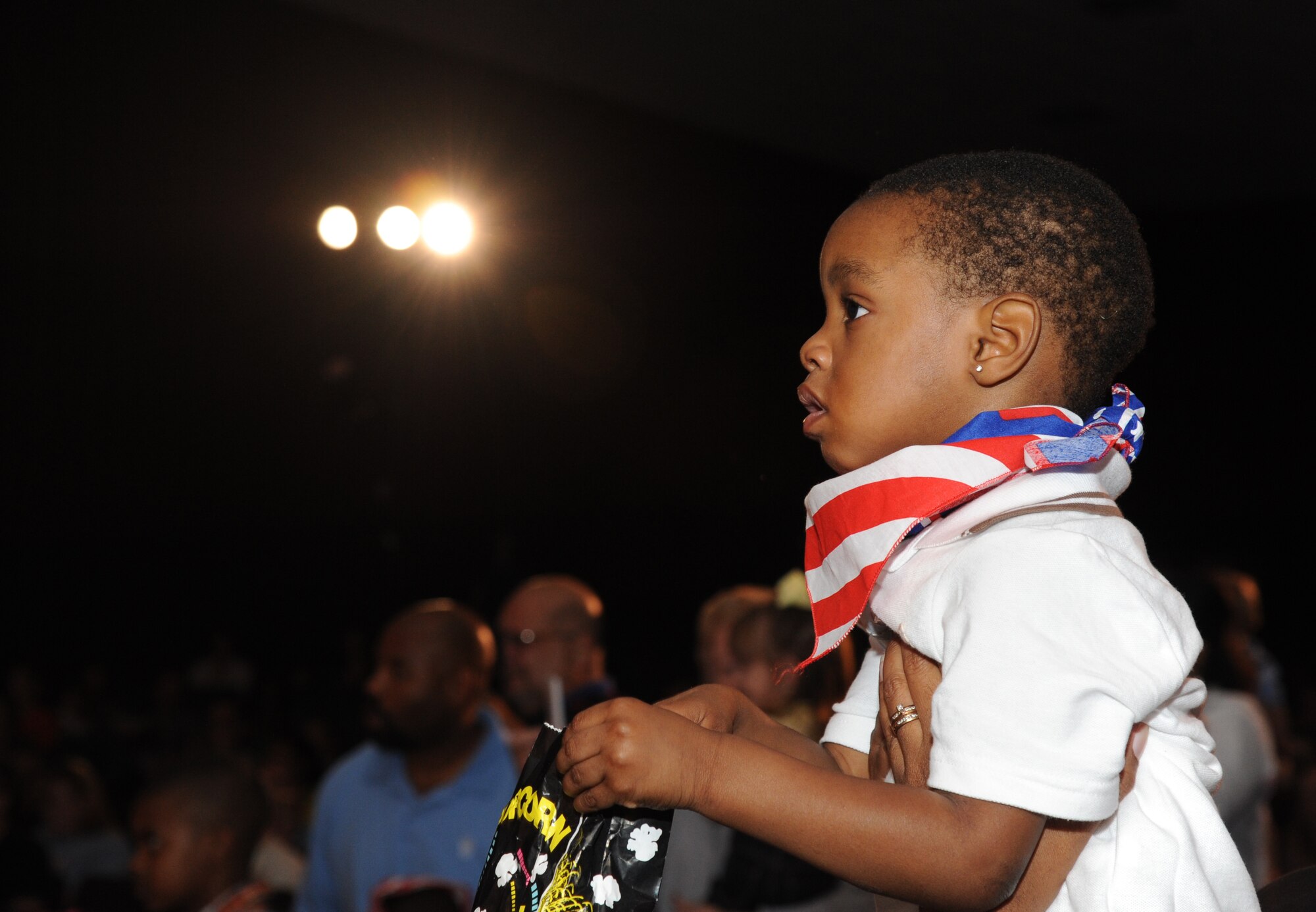 Two-year-old Roosevelt Metcalf, Jr., son of Ashley and Petty Officer 3rd Class Roosevelt Metcalf, Naval Mobile Construction Betallion, Gulfport, Miss., wears a USO bandana around his neck while he eats popcorn and watches  production of the Sesame Street/USO Experience for Military Families Oct. 9, 2012 at the Welch Theater, Keesler Air Force Base, Miss.  The 45-minute family-oriented event hosted by the 81st Force Support Squadron includes a character named Katie who is a military child.  With the help of her Sesame pals, Katie learns to deal with her fears and excitement about relocating.  The show emphasizes the importance of adjusting to change and the power of friendship.  (U.S. Air Force photo by Kemberly Groue)