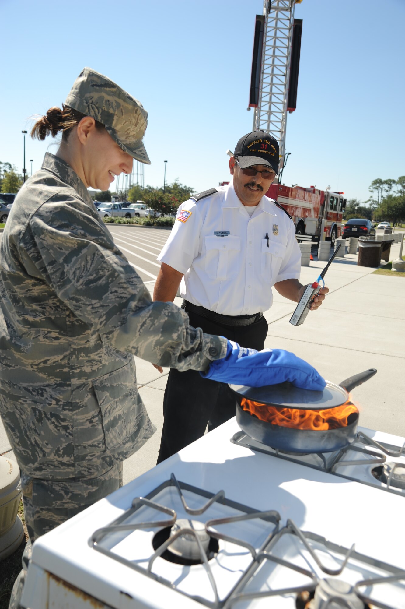 Second Lt. Rebecca Dreyer, 81st Surgical Operations Squadron, demonstrates how to safely put out a stove fire in a pan while being watched by David Tijerina, 81st Infrastructure Division firefighter, Oct. 9, 2012, outside of the Exchange at Keesler Air Force Base, Miss.  Throughout fire prevention week the Keesler Fire Department conducted random fire drills, toured various facilities with Sparky the Fire Dog, passed out fire safety handouts and fire hats for children and provided stove and fire extinguisher demonstrations.  The week–long event will end with an open house at the fire station 10 a.m. to 2 p.m. Oct. 13.  (U.S. Air Force photo by Kemberly Groue)