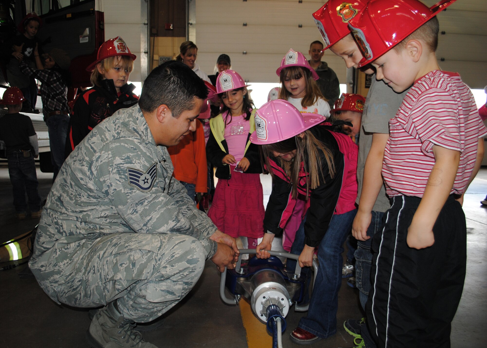 Staff Sgt. Robert Lysholm, 341st Civil Engineer Squadron fire fighter, helps Loy Elementary School kindergarteners pick up the Jaws of Life to see how heavy they are during the school’s tour of the Fire Department on Oct. 5.  During the tour, the kindergarteners were allowed to see the inside of a few fire department vehicles and meet Sparky the Fire Dog.  (U.S. Air Force photo/Airman 1st Class Cortney Paxton)