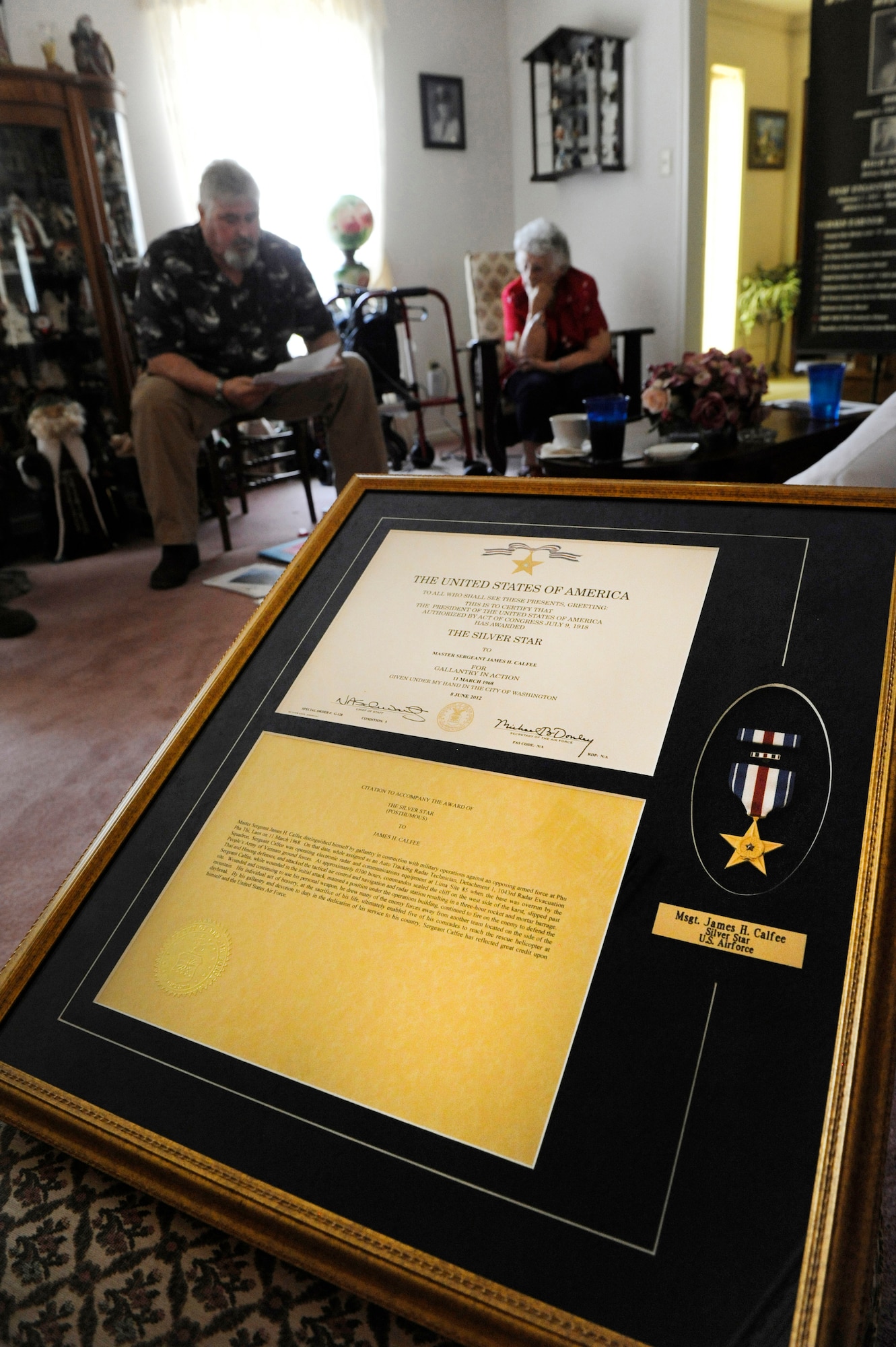 A framed Silver Star Medal and citation sits in the foreground as Rosalie Bacicia, back right, sister of the late Master Sgt. James Calfee, and Delton Kayga, a brother-in-law, look at documents about Calfee in Houston, Texas, Aug. 22, 2012. Calfee, who was posthumously awarded the Silver Star Medal, was killed in action in Laos in 1968. (U.S. Air Force photo/Val Gempis)