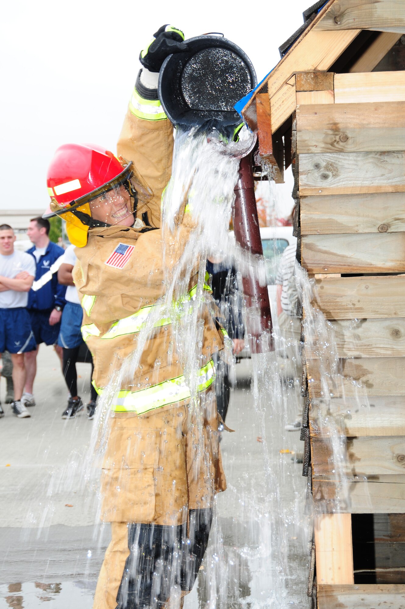 Sarah Hooper, 100th Force Support Squadron ‘Cheeky Chicks’ team, pours water onto the roof of a simulated house as her teammates bring buckets of water from a pool during a fire muster at the 100th Civil Engineer Squadron Fire Department Oct. 11, 2012, at RAF Mildenhall, England. During the final part of the fire muster event, teams had to collect water and pour it onto the house, when it then poured down a drainpipe and into a large container, where it had to reach a certain mark. Six teams participated in the event, which included a hose pull, dry hose advancement, mannequin rescue and Keiser sled. (U.S. Air Force photo by Karen Abeyasekere/Released)