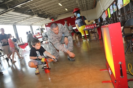 Aaron Wholly, the son of Master Sgt. Arthur Wholly, assigned to Joint Base San Antonio-Randolph, simulates extinguishing a fire while Airman 1st Class Brett Olsen, 902nd Civil Engineer Squadron firefighter, assists him at a Fire Prevention Week observance Oct. 13 at Randolph. (U.S. Air Force photo by Josh Rodriguez)  