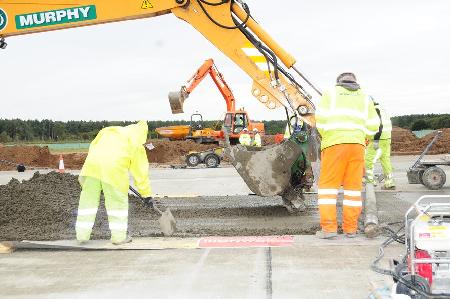 Contractors lay cement using an excavator, as part of the runway extension Oct. 5, 2012, at RAF Mildenhall, England. The pavement-quality concrete is laid to a thickness of 380 millimeters. Once dried, a saw is used to cut lines in the concrete, before being filled with a special sealant which allows it to expand and contract, to avoid cracking. (U.S. Air Force photo by Karen Abeyasekere/Released)
 
