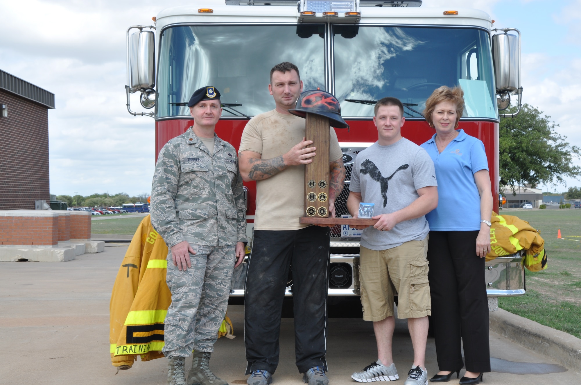 GOODFELLOW AIR FORCE BASE, Texas – (left to right) Maj. Dennis Turriff, 17th Security Forces Squadron commander, Tech. Sgt. Ray Hagenmeister, 17th Security Forces combat arms, Staff Sgt. Vernon Boyd, 17th Security Forces flight sergeant, and Staff Sgt. Jeremy Smith (not pictured), 17th Security Forces report and analysis, are presented the trophy for the Firefighter Muster by Shelene Black, 1st Community Credit Union Goodfellow Air Force Base branch manager, at the Fire Station Oct. 12. Their team, Defenders, placed first with a time just under eight minutes. (U.S. Air Force photo/ Airman 1st Class Joshua Edwards)