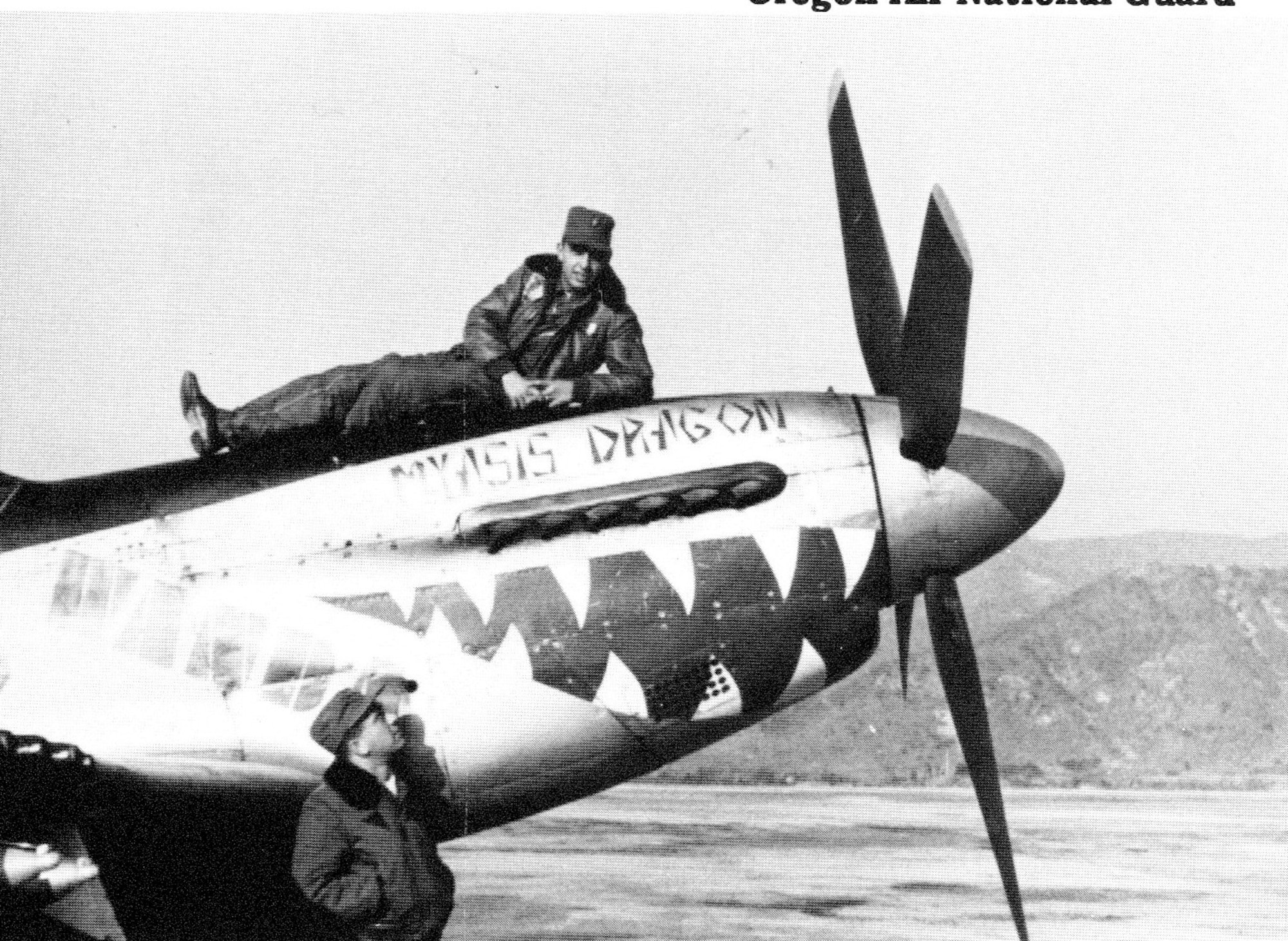Ore ANG pilot Ernest Wakehouse strikes a leisurely pose atop the nose of a Mustang in Korea during a break in operations.  But combat flying wasn’t  leisurely at all and the name on the plane, ”Myasis Dragon,” described how he felt at times during his combat tour.  Another F-51 pilot, possibly Wallace Parks, looks on.