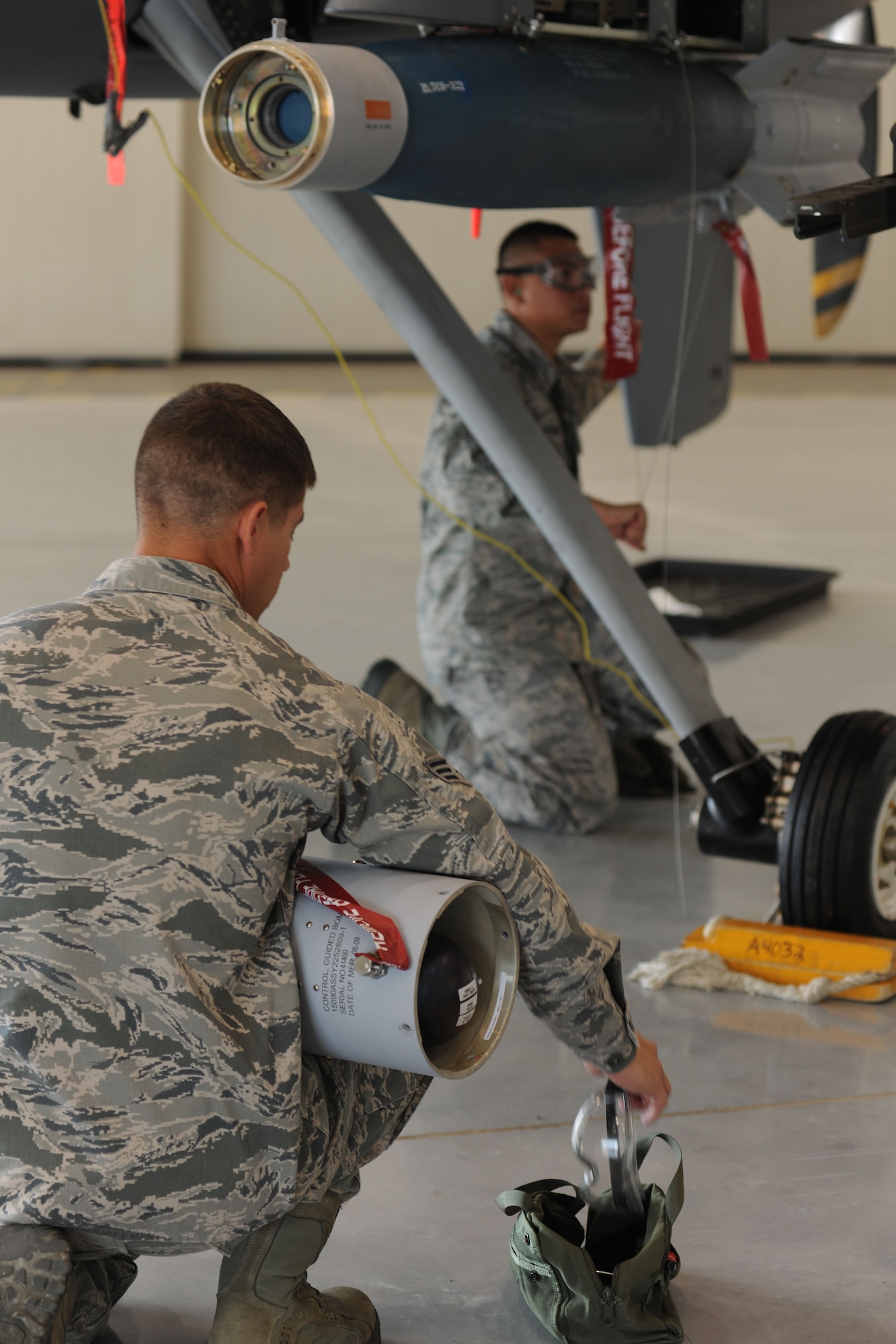 A weapons loader from the 432d Maintenance Group reaches for safety goggles during the loading of a GBU-12 Paveway II laser guided munitions on a MQ-9 Reaper remotely piloted aircraft (RPA) while another safety wires the munitions into place, Oct. 5, 2012, at Creech Air Force Base, Nev. The crew was competing in the 432d MXG load crew of the quarter competition in which two three-man weapons loading teams from two maintenance units at Creech to compete against each other. (U.S. Air Force photo by 432d Wing/432d Air Expeditionary Wing Public Affairs)