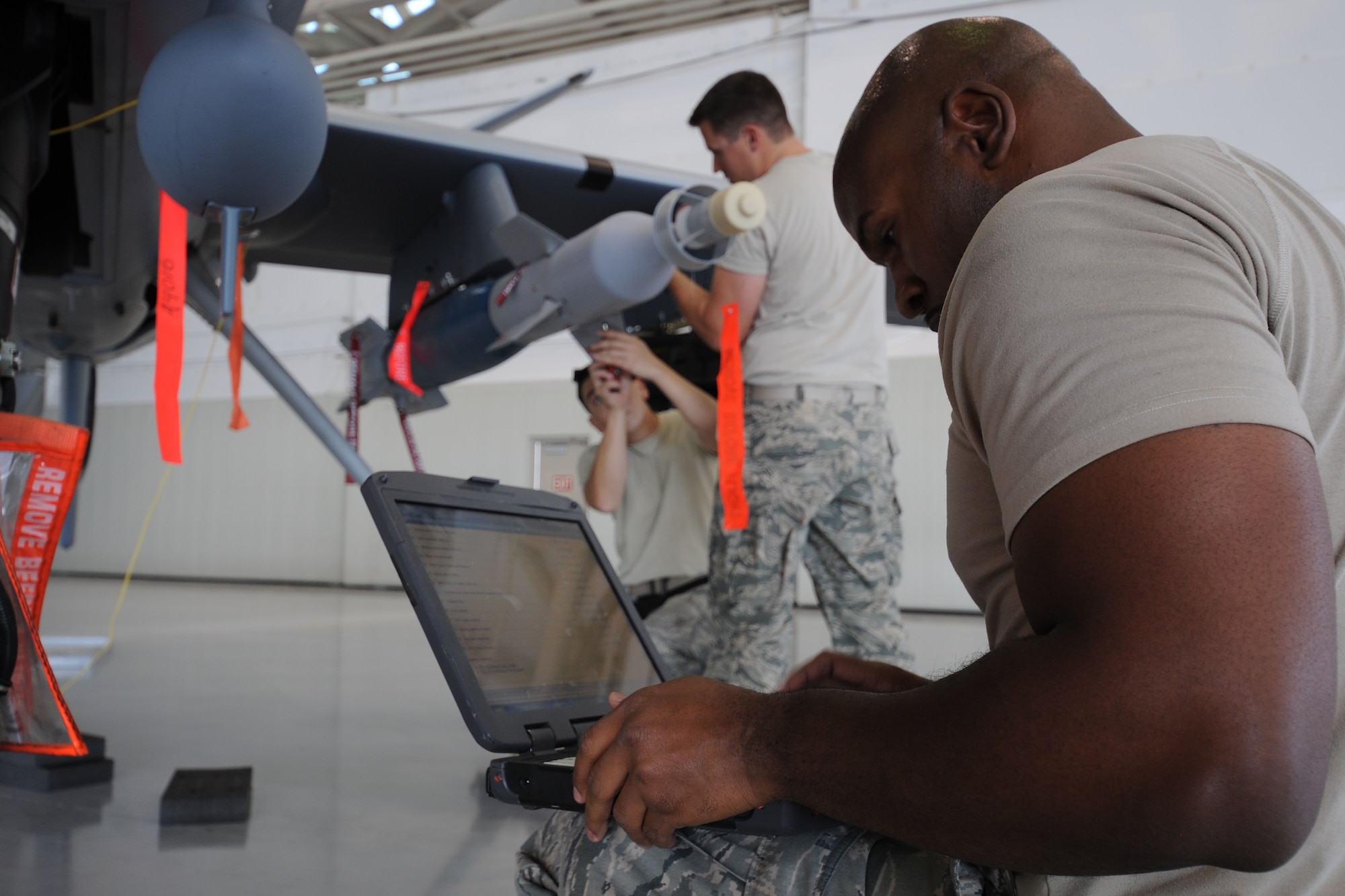 Weapons loaders assigned to the 432d Aircraft Maintenance Group work together to load a GBU-12 Paveway II laser guided munitions on a MQ-9 Reaper while the team lead reviews an electronic technical order for accuracy during the 432d MXG load crew of the quarter competition, Oct. 5, 2012, at Creech Air Force Base, Nev. The three-man weapons loading teams are evaluated on a variety of technical aspects to include safety, use of tools, technical order violations and overall time. (U.S. Air Force photo by 432d Wing/432d Air Expeditionary Wing Public Affairs)
