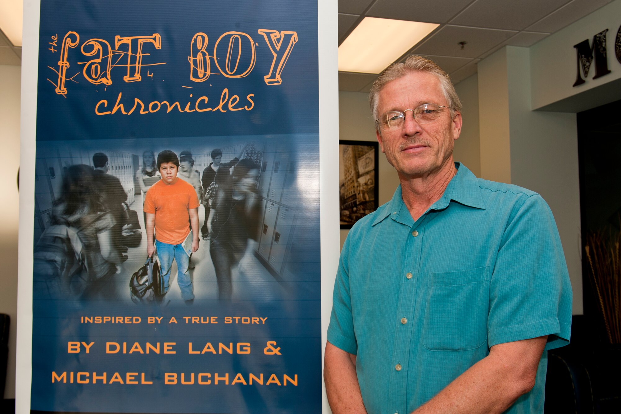 Michael Buchanan, Tin Roof Productions producer, stands next to a promotional poster for the film The Fat Boy Chronicles at the Moody Air Force Base, Ga., auditorium, Oct. 11, 2012. Buchanan, who co-wrote and co-produced the novel and film, visited Moody to help spread knowledge on bully prevention, childhood obesity and the importance of education. This was his first time visiting a military base during his stateside tour. (U.S. Air Force photo by Staff Sgt. Jamal D. Sutter/Released)  
