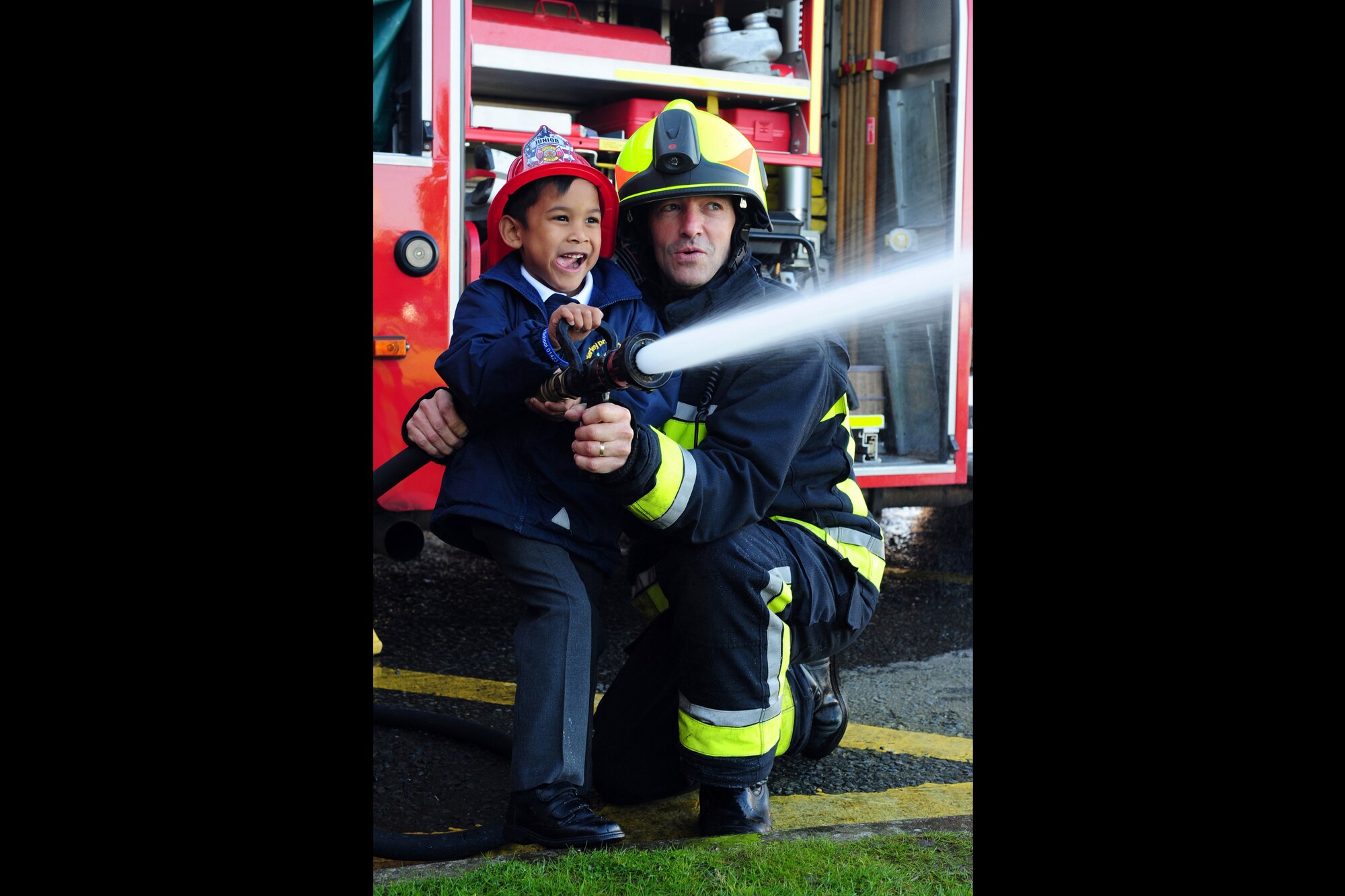 RAF MENWITH HILL, United Kingdom - Owen Taylor, a Menwith Hill Station firefighter, helps Mitchell Currie, an early year student from Darley Primary School, shoot a fire hose at targets during the Fire Prevention Week event at the Fire Station Oct. 9. When fire strikes, a home can be engulfed in flames and filled with smoke in minutes so it is important for families to have an escape plan and know about fire safety. This year's Fire Prevention Week theme is "Have two ways out" which focuses on the importance of fires escape planning and practice. For more information on Fire Prevention Week, or for tips on how to keep your family safe visit www.nfpa.org. (U.S. Air Force photo by Staff Sgt. Debbie Lockhart)