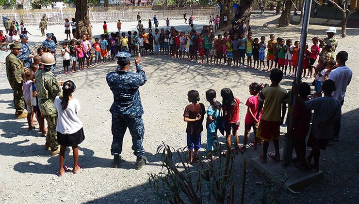 Marines and sailors with the 15th Marine Expeditionary Unit and Peleliu Amphibious Ready Group sing and dance with Timorese children after they presented books, school supplies and sporting goods to their elementary school in Liquicia, Timor-Leste, Oct. 13. The donations were part of a community relations program supporting Exercise Crocodilo 2012, a U.S./Timor-Leste event promoting interoperability and regional stability.