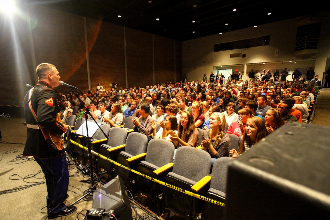 Lance Cpl. David Corderman of Richmond, Va., sings in front of hundreds of high school students. He and two other Marines within the band took the initiative to come together and form the 2nd Marine Division rock band. 