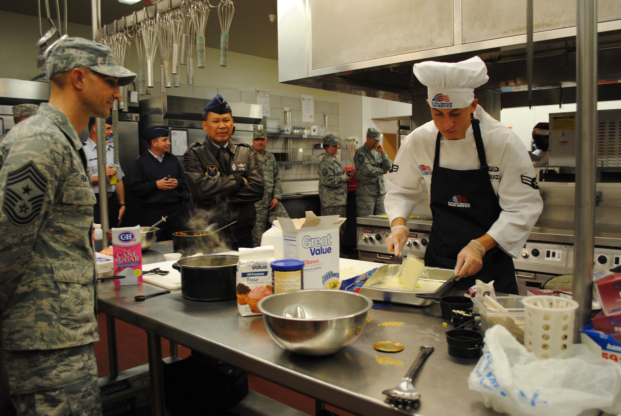 Chief Master Sgt. Frank Fidani, 341st Missile Wing command chief, left, and Col. H.B. Brual, 341st MW commander, observe Airman 1st Class Dimitris Griffin, 10th Missile Squadron missile chef, as he butters a pan. Griffin’s partner was Airman 1st Class Justin Ruiz, and their signature dish was pumpkin macaroni and cheese, and cheesecake cupcakes. (U.S. Air Force photo/Airman 1st Class Katrina Heikkinen)