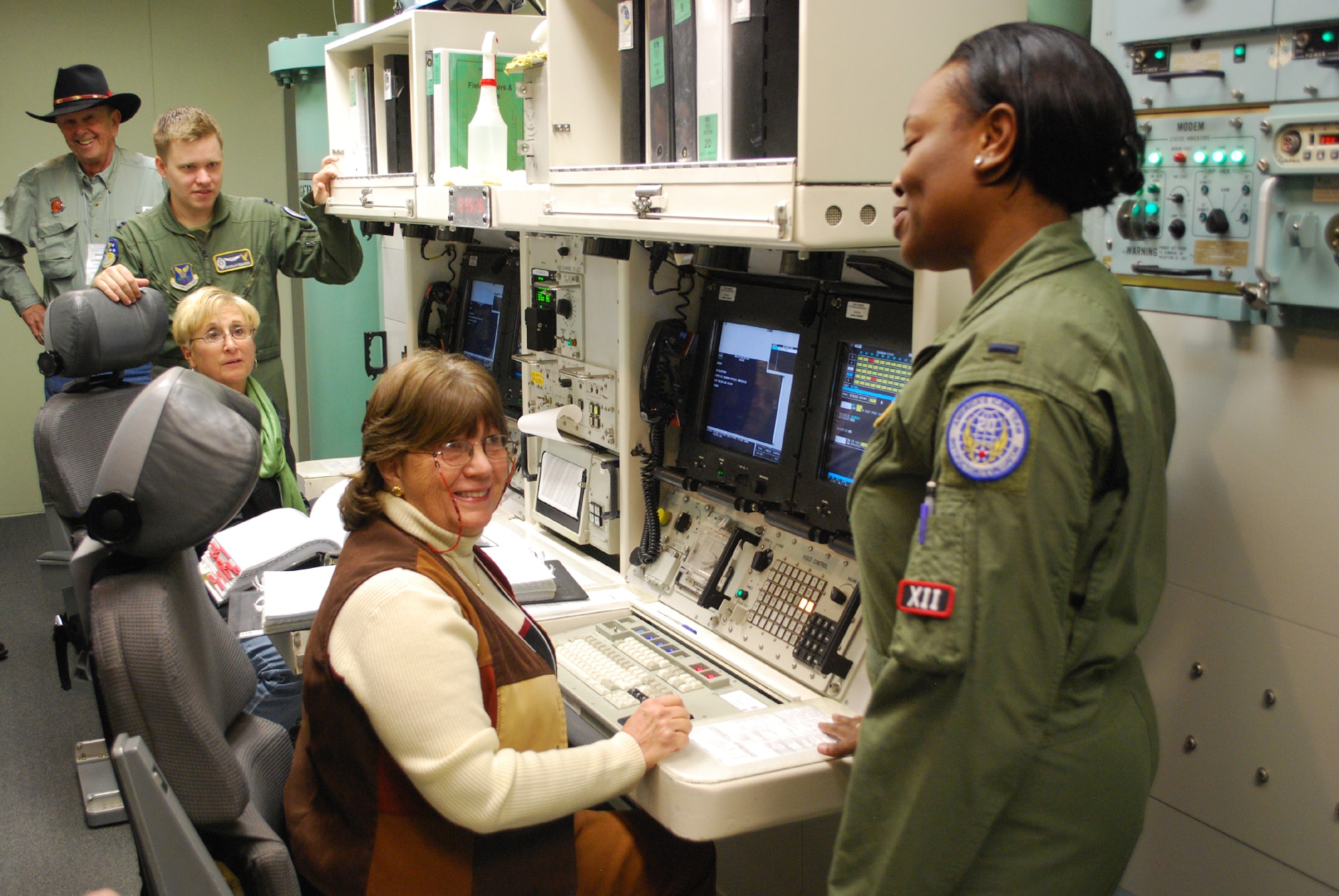 1st Lt. Arielle Wallace, 341st Operations Support Squadron instructor deputy combat crew commander, far right, and Capt. Nicholas Edwards, 341st OSS instructor combat crew commander, explain the next step of a “key turn” to two members who toured the Missile Procedures Trainer on Oct. 11 during the 50th Anniversary celebration.  Both women operating the MPT are spouses to retired Air Force members who once operated the same systems; on the left consol is Kay Williams, wife to retired Col. Ronald Williams, and on the right consol is Mickey Livingston, wife to retired Col. Doug Livingston (pictured in background).  (U.S. Air Force photo/Airman 1st Class Cortney Paxton)