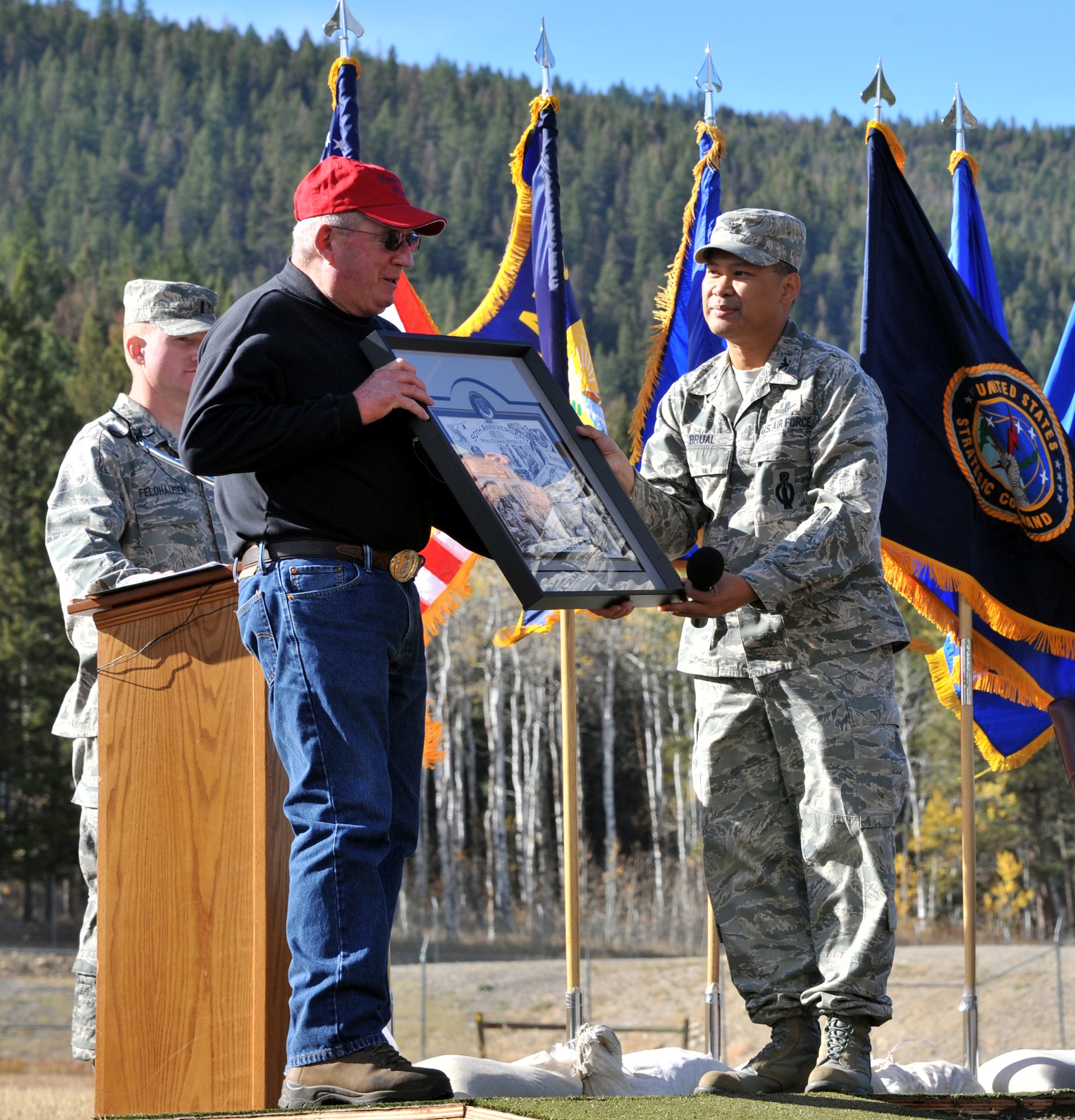 Col. H.B. Brual, 341st Missile Wing commander, presents retired Col. Stephen Heppell with a framed 50th Anniversary lithograph to thank him for his support of the celebration held on Oct. 13. Heppell owns the land that A-06 is housed on.  1st Lt. Lee Feldhausen, emcee for the event, looks on. (U.S. Air Force photo/John Turner)