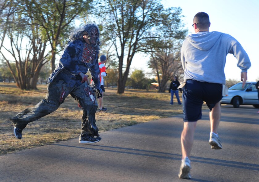 An Airman dressed as a zombie chases down participants of the Zombie 5K at Cannon Air Force Base, N.M., Oct. 19, 2012. Personnel volunteered to be transformed into their undead alter egos to hunt down fellow Airmen during the run that encouraged Air Commandos to get involved in the local Air Force First Sergeant’s Association chapter. (U.S. Air Force photo/Airman 1st Class Ericka Engblom)