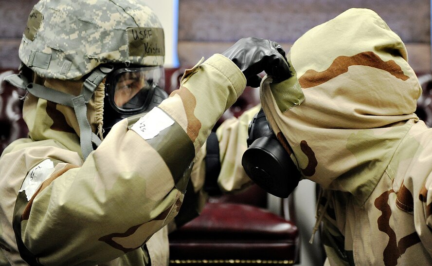 Chaplain (Capt.) Krista Ingram, 375th Air Mobility Wing, assists Airman 1st Class Lindsay Kelly, 375th Air Mobility Wing broadcaster, by ensuring her hood is covering her gas mask correctly during a simulated attack while participating in an Operational Readiness Exercise Oct. 18 at Scott Air Force Base, Ill. The 375 AMW is participating in an exercise designed to test their ability to survive and operate in a hostile or chemical environment. (U.S. Air Force photo/Airman Kris Lynch)