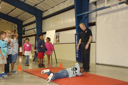 Kenny Shepard, 902nd Civil Engineer Squadron firefighter and emergency medical technician, oversees a Randolph Elementary School student demonstrating the proper stop, drop and roll procedure during the annual Fire Prevention Week demonstration Oct. 10 at Joint Base San Antonio-Randolph. Fire Prevention Week was established to commemorate the Great Chicago Fire of 1871 that killed more than 250 people, left 100,000 homeless, destroyed more that 17,400 structures and burned more than 2,000 acres.  (U.S. Air Force photo by Josh Rodriguez)