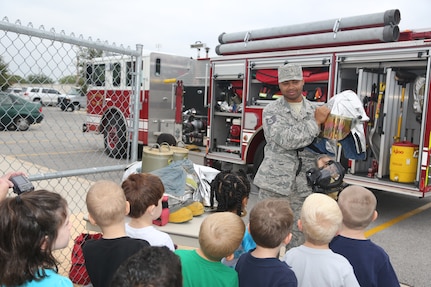 Staff Sgt. Garcia Tarver, 902nd Civil Engineer Squadron Fire Emergency Service B shift crew chief, demonstrates firefighters' personal protective equipment to a class of students from Randolph Elementary School at the annual Fire Prevention Week demonstration Oct 10. at Joint Base San Antonio-Randolph. Fire Prevention Week was established to commemorate the Great Chicago Fire, the 1871 conflagration that killed more than 250 people, left 100,00 homeless, destroyed more that 17,400 structures and burned more than 2,000 acres. The fire began Oct. 8, but continued into and did most of its damage Oct. 9, 1871.  (U.S. Air Force photo by Josh Rodriguez)