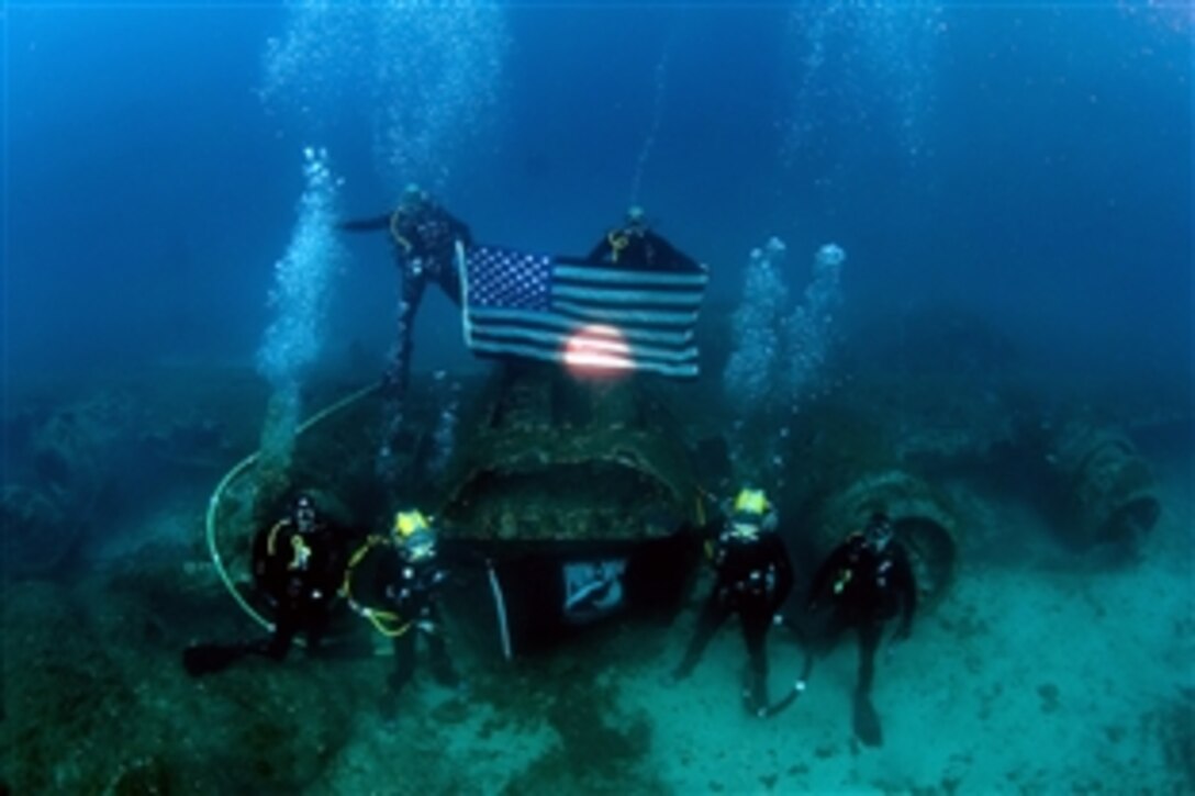 Navy divers, assigned to Mobile Diving and Salvage Unit 2, Company 4, and the Joint POW/MIA Accounting Command, stand with the American flag, and the POW/MIA flag on the wreckage of a B-17 bomber that was shot down and sank during World War II during a dive Oct. 19, 2012. The team is deployed alongside JPAC aboard the USNS Grapple as part of a 30-day underwater recovery mission for an unaccounted-for service member who went missing during the crash. 