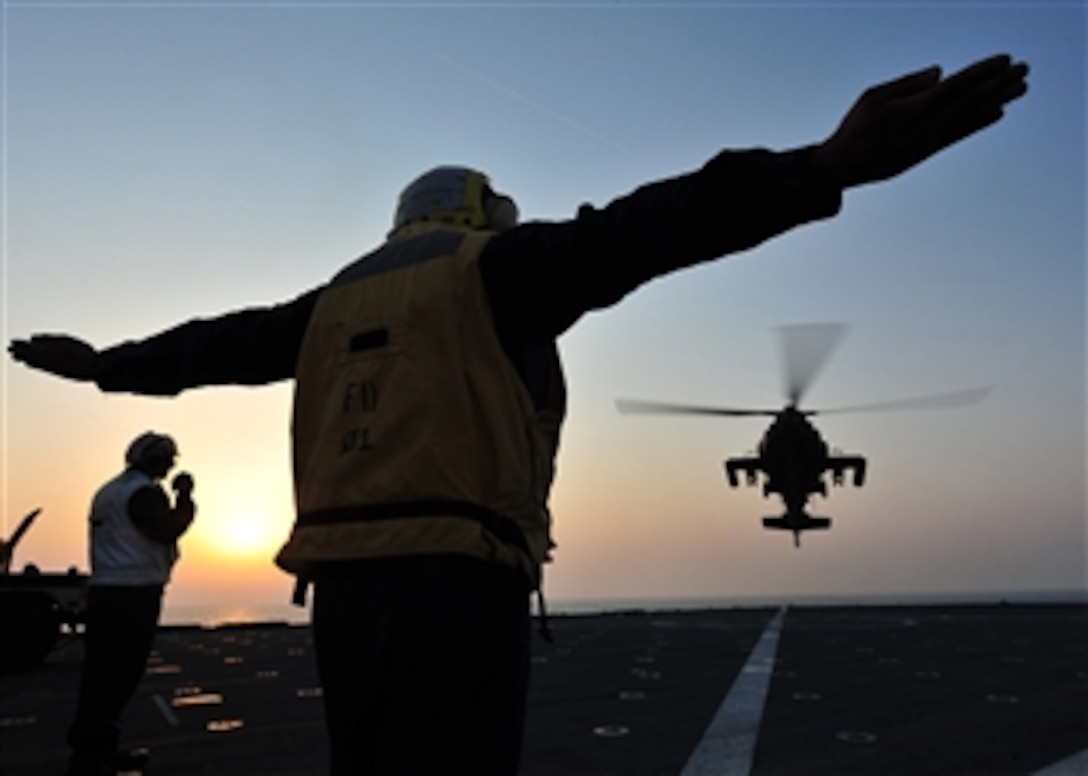 U.S. Navy Petty Officer 3rd Class Jean Petitfrere signals a U.S. Army AH-64 Longbow Apache helicopter to land on the flight deck of the USS Gunston Hall (LSD 44) as the ship steams in the Arabian Sea on Oct. 9, 2012.  Gunston Hall and the embarked 24th Marine Expeditionary Unit are part of the Iwo Jima Amphibious Ready Group which is deployed in support of maritime and theater security operations in the U.S. 5th Fleet area of responsibility.  