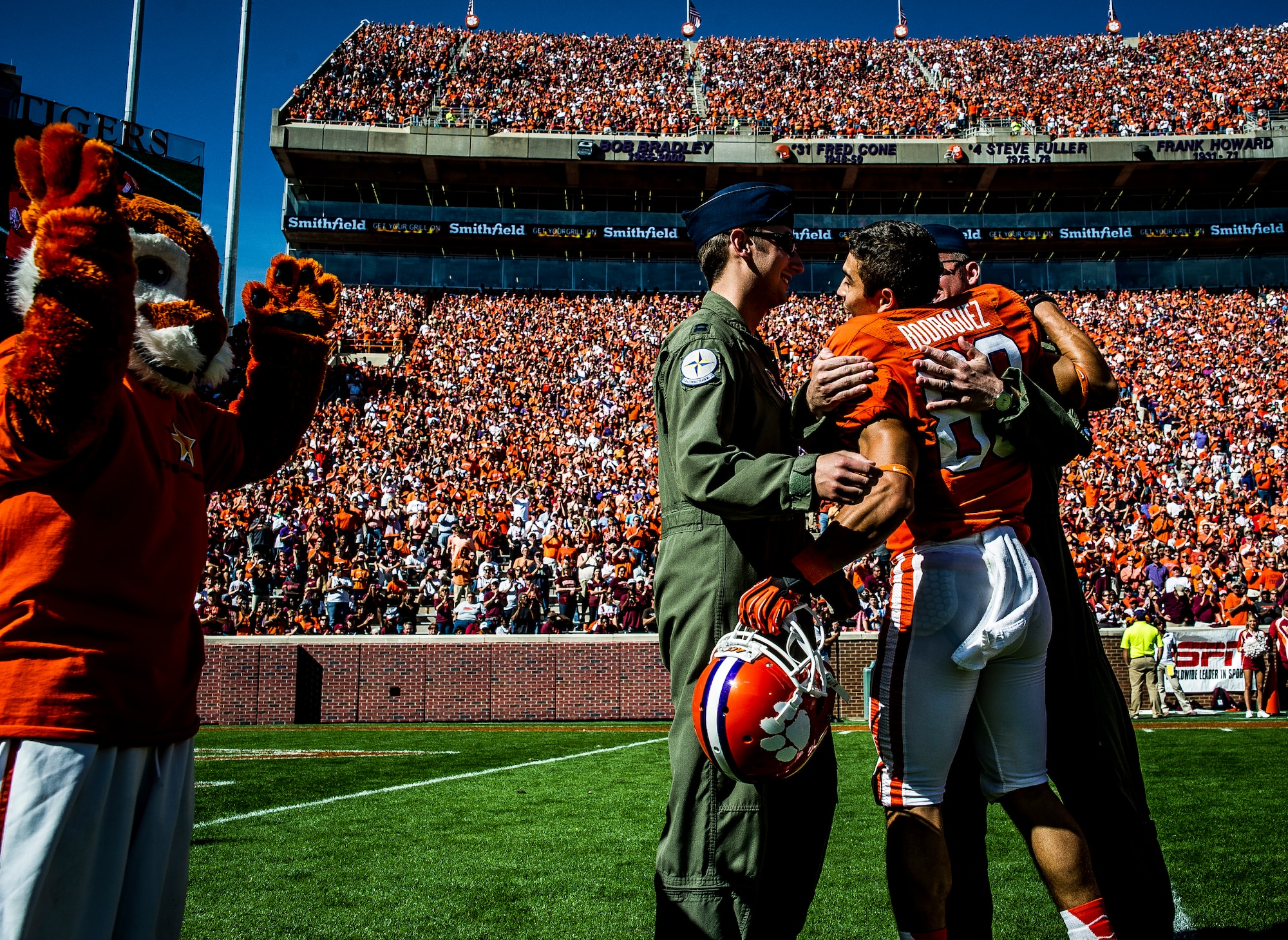 Former Army Sgt. Daniel Rodriguez, now a wide receiver for the Clemson tigers, hugs Capt. Justin Kulish (left) and Capt. Michael Polidor (right), B-2 Bomber pilots from Whiteman Air Force Base, Mo., during a ceremony Oct. 20, 2012, at Memorial Stadium, Clemson S.C. The two pilots were recognized for their efforts providing close-air support during an insurgent ambush of Command Outpost Keating in October 2009. Rodriguez was deployed to the outpost during the attack. (U.S. Air Force photo/Senior Airman Dennis Sloan)