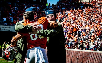 Former Army Sgt. Daniel Rodriguez, now a wide receiver for the Clemson tigers, hugs Air Force Capt. Justin Kulish (left) and Air Force Capt. Michael Polidor (right), both B-2 Bomber pilots from Whiteman Air Force Base, Mo., during a ceremony Oct. 20, 2012, at Memorial Stadium, Clemson S.C. The two pilots were recognized for their efforts providing close-air support during an insurgent ambush of Command Outpost Keating in October 2009. Rodriguez was deployed to the outpost during the attack. (U.S. Air Force photo/Senior Airman William O’Brien)