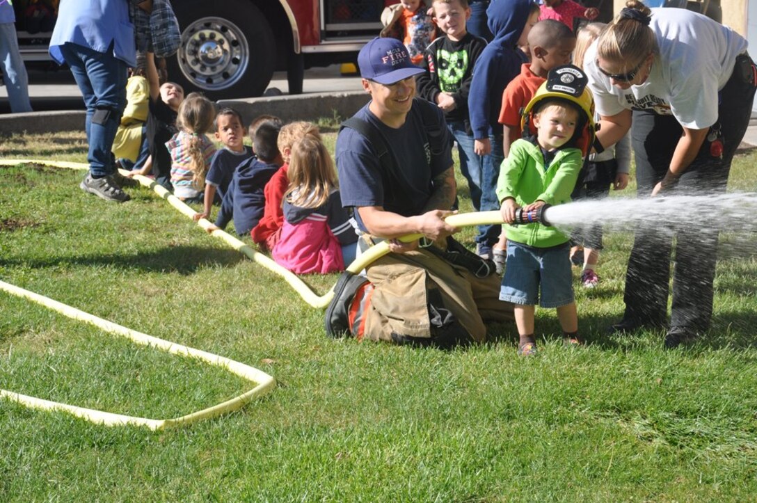 Paul Aguilar, a firefighter aboard Marine Corps Logistics Base Barstow, Calif., holds a hose as children from the Child Development Center aboard the base take turns spraying the water, Oct. 9. The CDC took their three and four-year-old children on a field trip and tour of the fire station in support of Fire Prevention Week 2012.