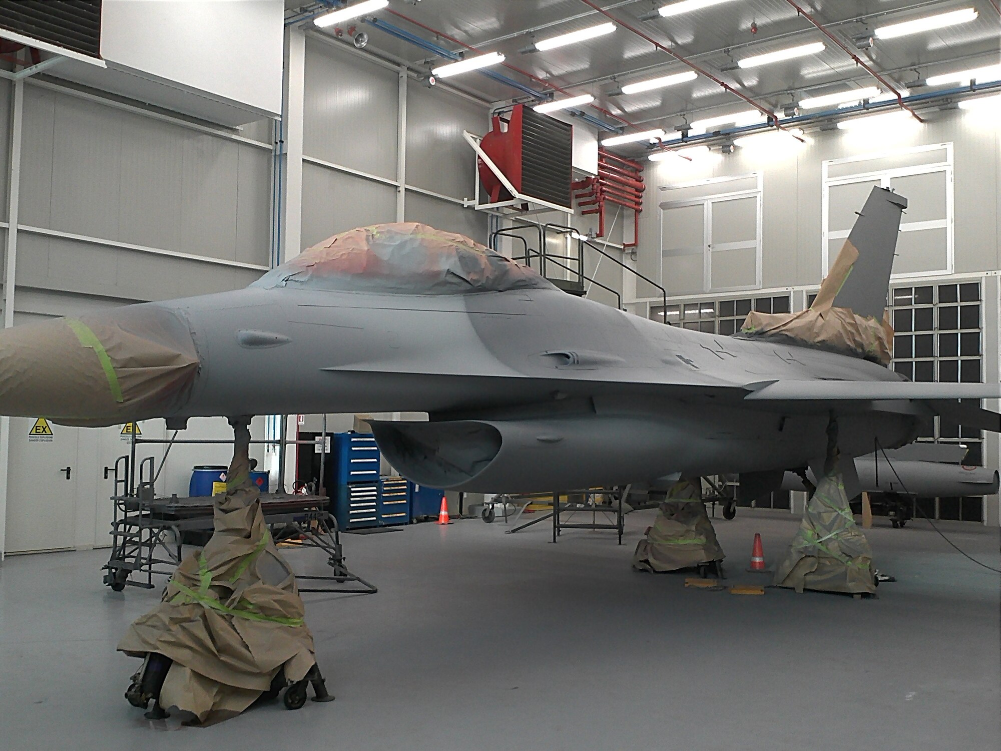 An F-16 Fighting Falcon is prepped for stenciling during a repaint in the new Corrosion Control Facility at Aviano Air Base, Italy.  The new facility allows personnel assigned to the aircraft structural maintenance corrosion control section the ability to conduct all aspects of corrosion control and treatment, to include sanding, media blasting, priming and painting and stenciling an entire F-16. (Courtesy Photo)