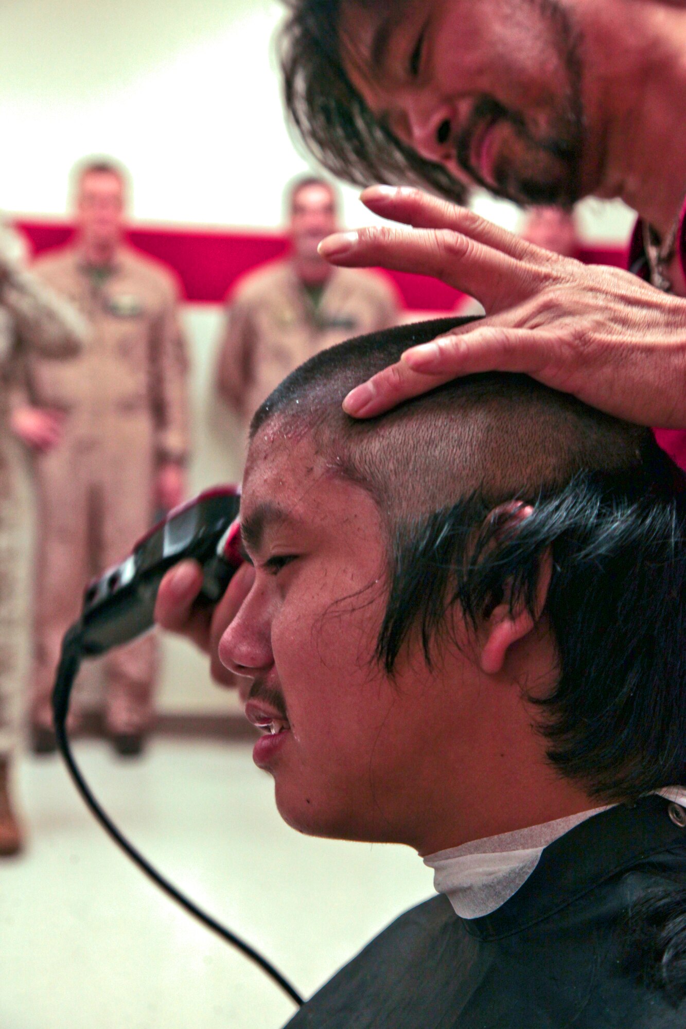 Marine All-Weather Fighter Attack Squadron 224, 225 and Marine Aircraft Group 12 Marines and sailors watch an Okkodo High School Marine Corps Junior Reserve Officer Training Corps cadet receive a high and tight haircut aboard Andersen Air Force Base Oct. 17, 2012. Sixteen VMFA(AW)-224, 225 and MAG-12 Marines and sailors visited Okkodo High School JROTC cadets and students.