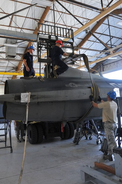 The 309th Aircraft Maintenance Group depot team from Hill prepares to lift the F-16 fuselage during the pack and crate operation. The “belly bands” are capable of lifting an aircraft with an approximate weight of 25,000 pounds. Depot teams deploy worldwide to perform specific and critical repairs on U.S. and foreign military fighter aircraft. (U.S. Air Force photo by Senior Airman Sandra Welch)