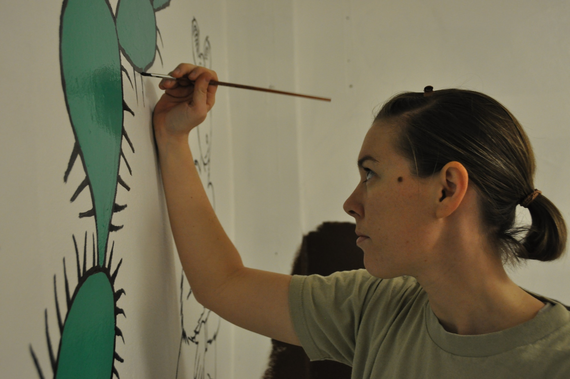 Staff Sgt. Olivia Updike, assigned to the 455th Expeditionary Operations Support Squadron, adds details to Dr. Seuss-inspired cacti in the Cat in the Hat Language Arts Center at Bagram Airfield, Afghanistan, October 23, 2012. Updike and other artistic volunteers give an average 20 hours per room to paint "Seussesque" murals on nearly every wall of the Language Arts Center. (U.S. Air Force photo/Tech. Sgt. Shawn McCowan)