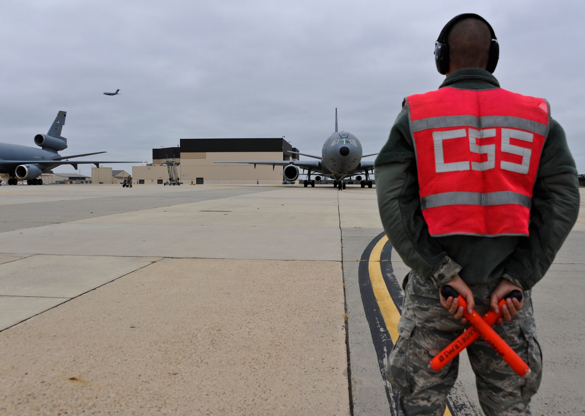 JOINT BASE MCGUIRE-DIX-LAKEHURST, N.J. -- Airman 1st Class Joseph Japp, 605th Aircraft Maintenance Squadron, waits to marshal a KC-10 Extender en route to the runway while a C-17 Globemaster III flies overhead Oct. 28, 2012. The 305th Air Mobility Wing's aircraft are being evacuated to alternate locations throughout the United States to avoid possible damage from Hurricane Sandy. (U.S. Air Force photo by Staff Sgt. David Carbajal/Released)