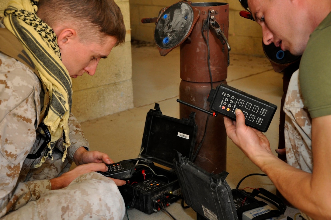 Sgt. Colin W. Gabriel, left, and Sgt. Zach M. Walker, right, air traffic controllers on the air station here, program the frequencies on a remote improvised explosive device during a field training exercise at Range 131 here Oct. 26.