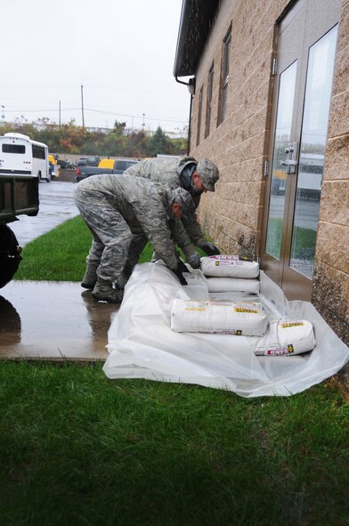 Senior Master Sgt. Christopher Shull and Master Sgt. Jeffrey Redline, 193rd Special Operations Wing, lay sandbags in front of building doors in hopes to prevent flooding that may be caused by hurricane Sandy. (U.S. Air Force Photo by Tech. Sgt. Mariko Bender)